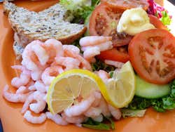 An orange plate with prawns, lemons, tomatoes, salad leaves and a slice of bread