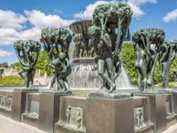 Copper statues of people holding up trees around a fountain
