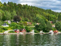 Small houses on the shore of a fjord in front of green forests