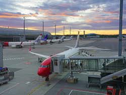 A white and red plane attached to a tunnel at the airport as the sun sets