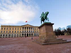 A large yellow building with several columns and a turquoise statue of a man riding a horse out front
