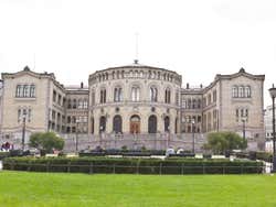 A grand grey building with a circular section in the centre behind a green park