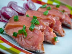 A plate of raw pink fish with chives on top and some red onion on the side