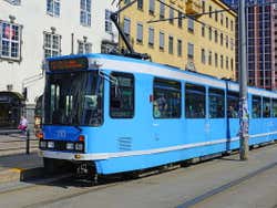 A small blue tram passing tall buildings in the city centre